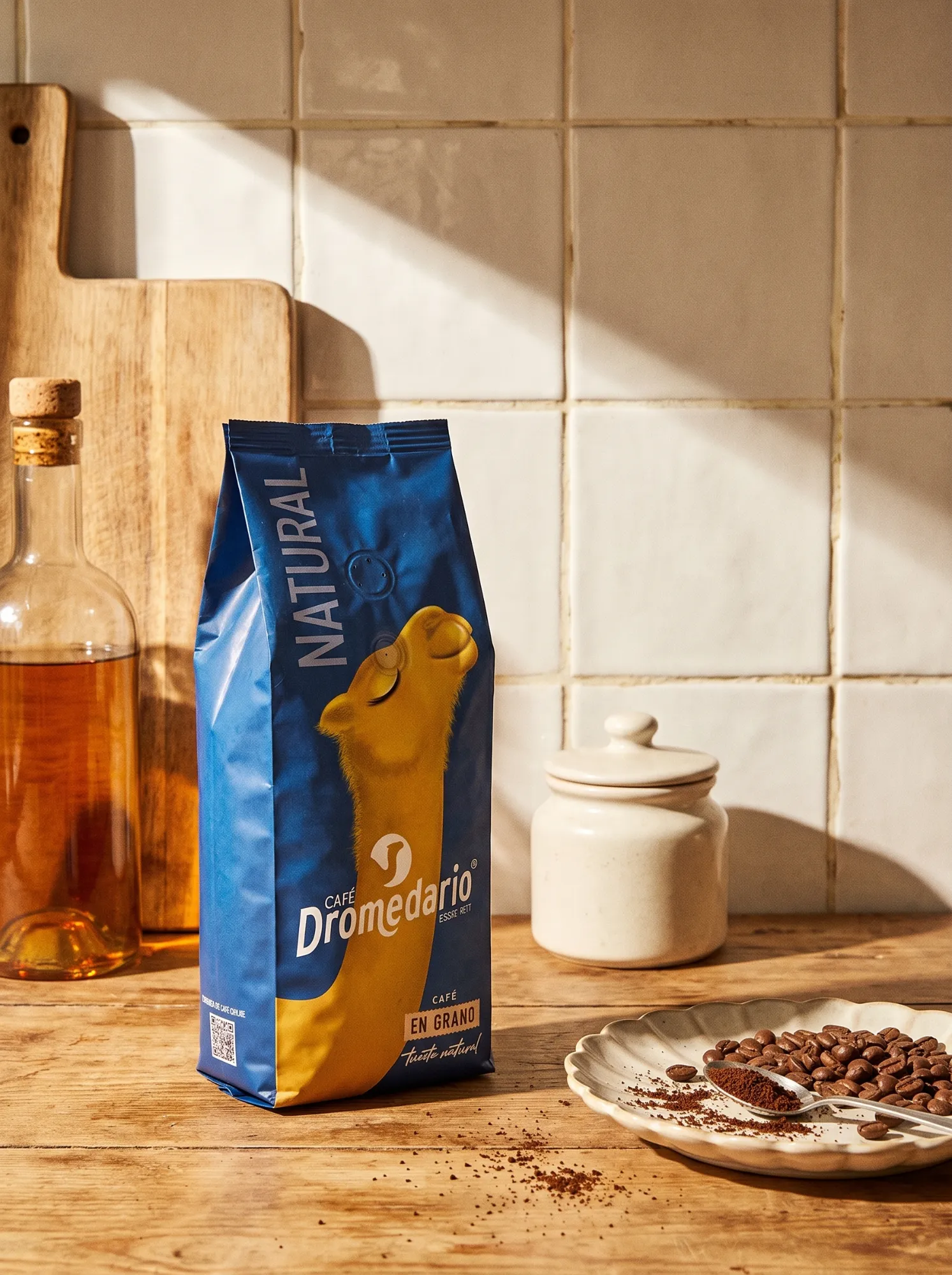 Bolsa de Café Dromedario Natural en grano sobre una encimera de madera, con luz de mañana, granos de café y un tarro de cerámica
